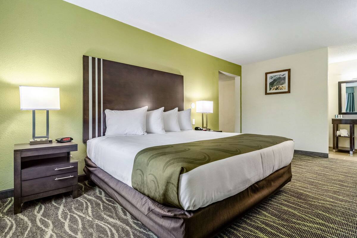 A hotel room with a large bed, two bedside tables, a nightstand, and a desk with a chair.