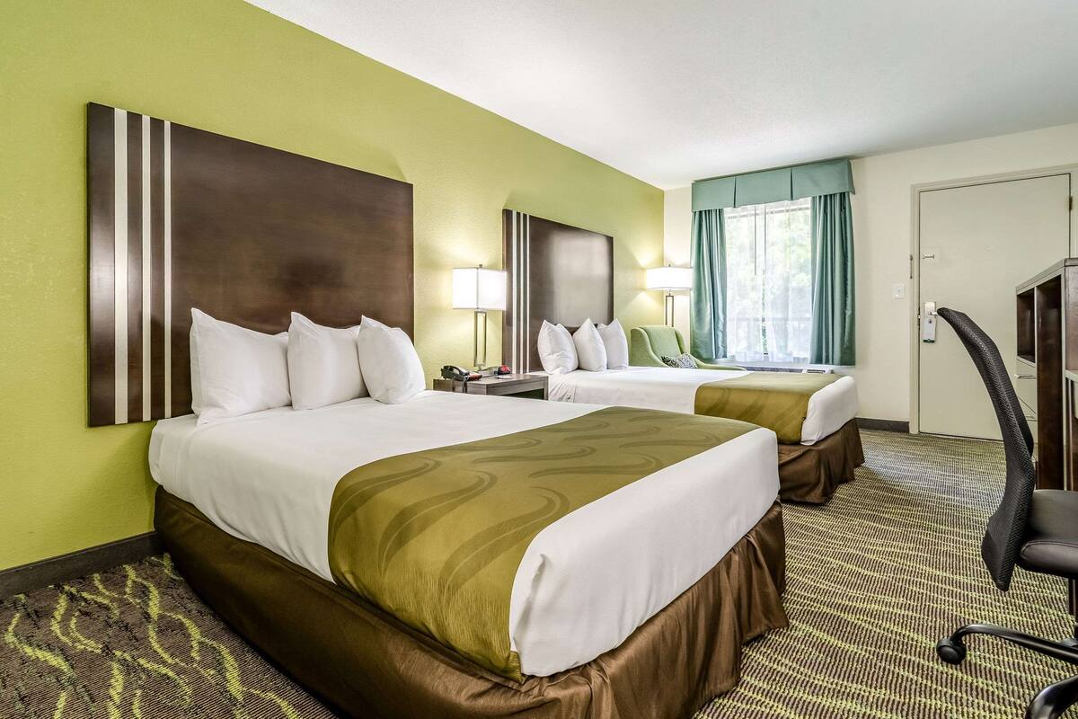 A hotel room with two beds, a desk, a chair, and a window with curtains.