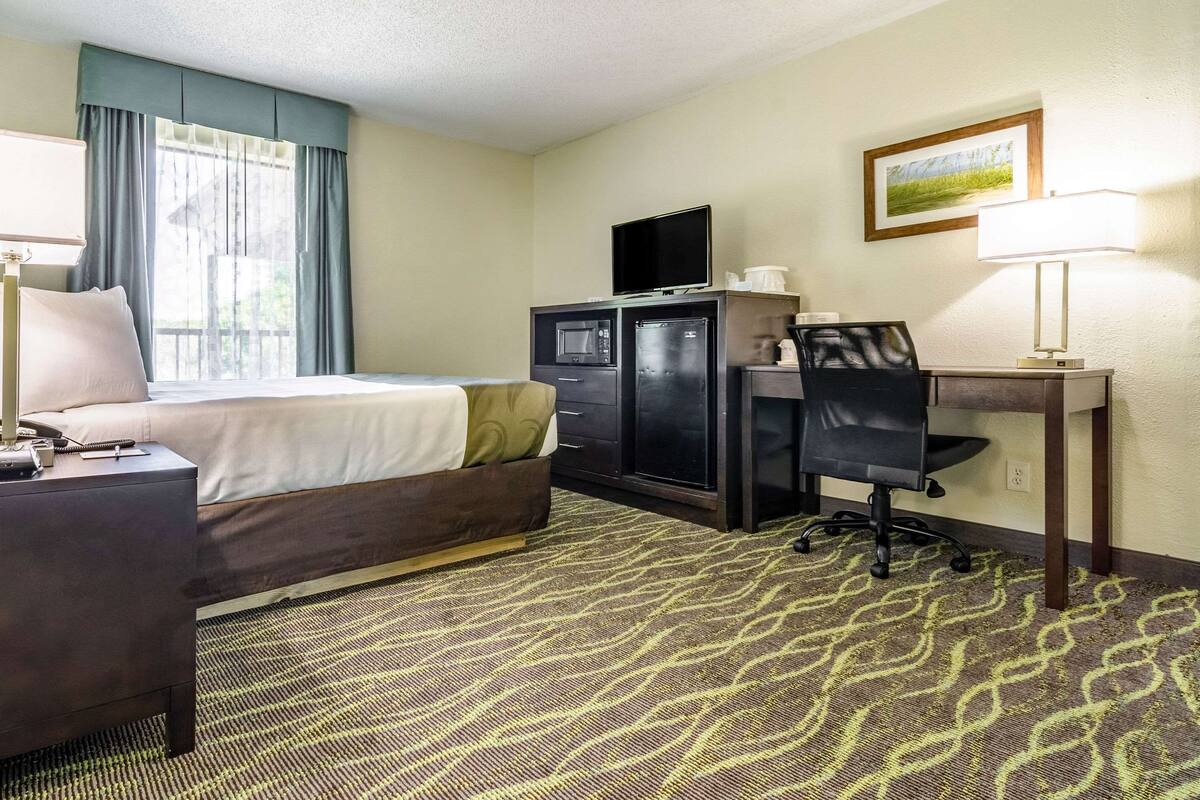 A hotel room with a bed, a desk with a computer, a microwave, and a refrigerator.