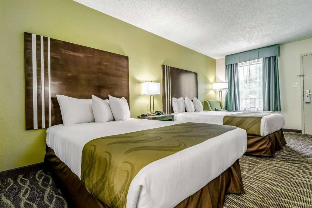 A hotel room with two beds, a large wall art piece, a lamp, and a window with curtains.
