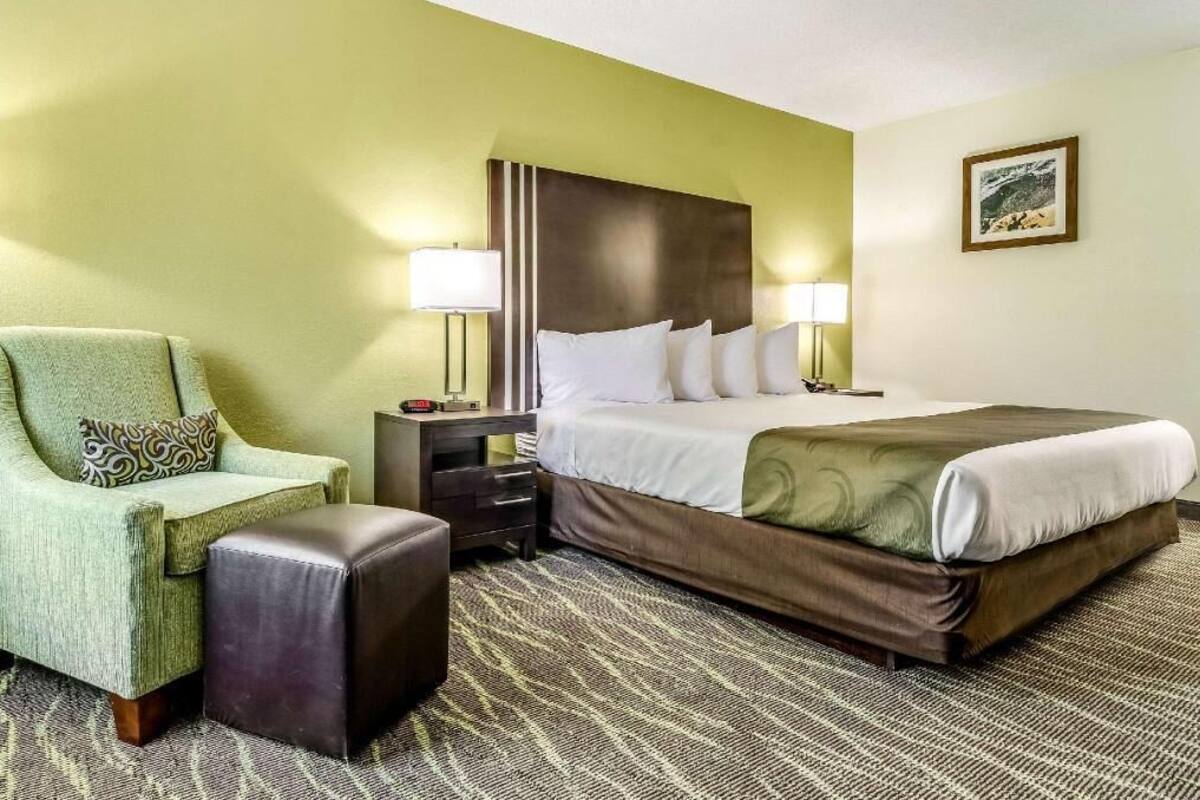 A hotel room with a bed, a chair, a nightstand, and a lamp.