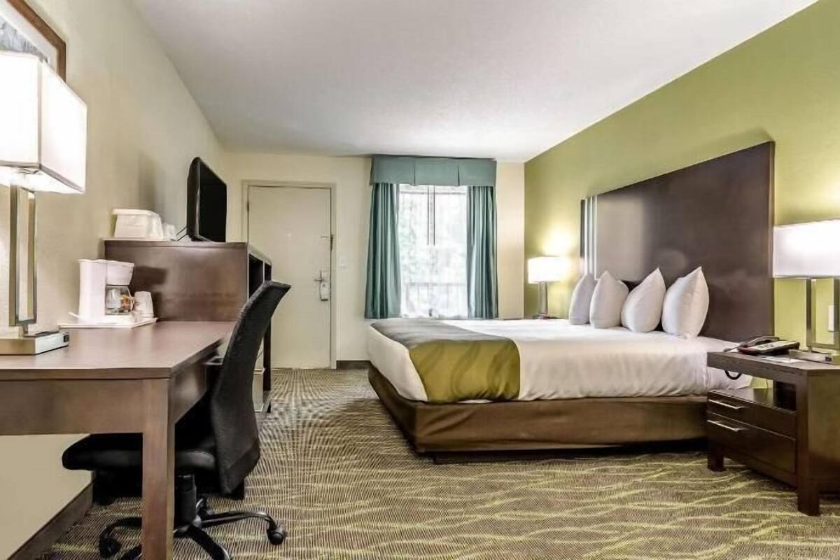 A hotel room with a bed, desk, chair, and a window with curtains.