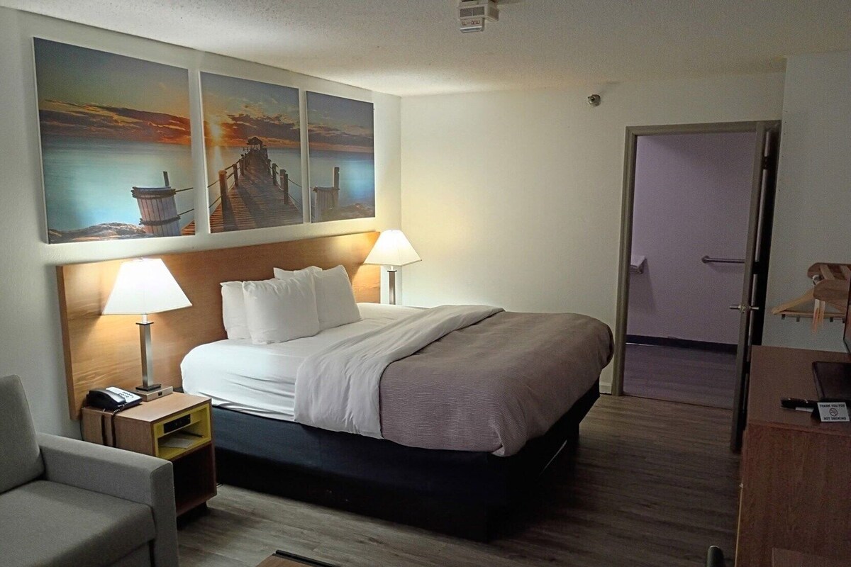 A hotel room with a bed, two bedside lamps, a desk, a chair, and artwork on the wall.