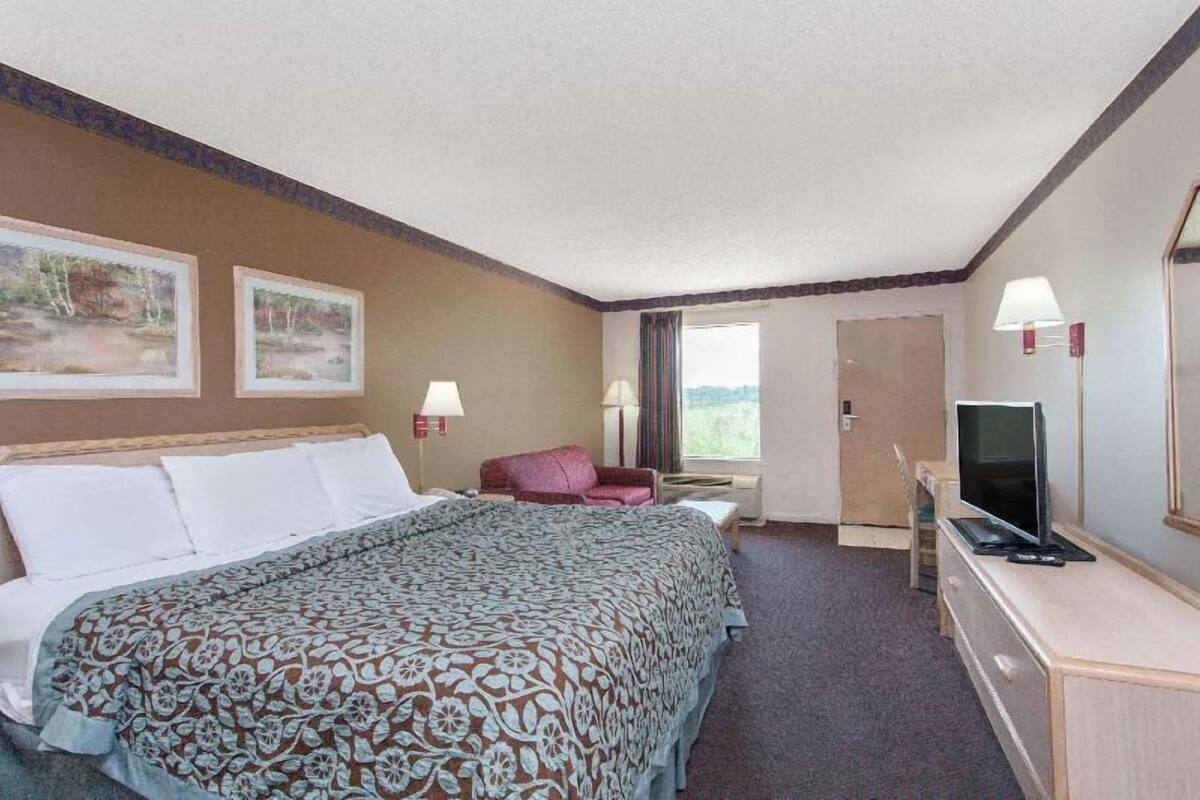 A hotel room with a bed, a desk with a TV, a chair, a window, and two wall-mounted lamps.