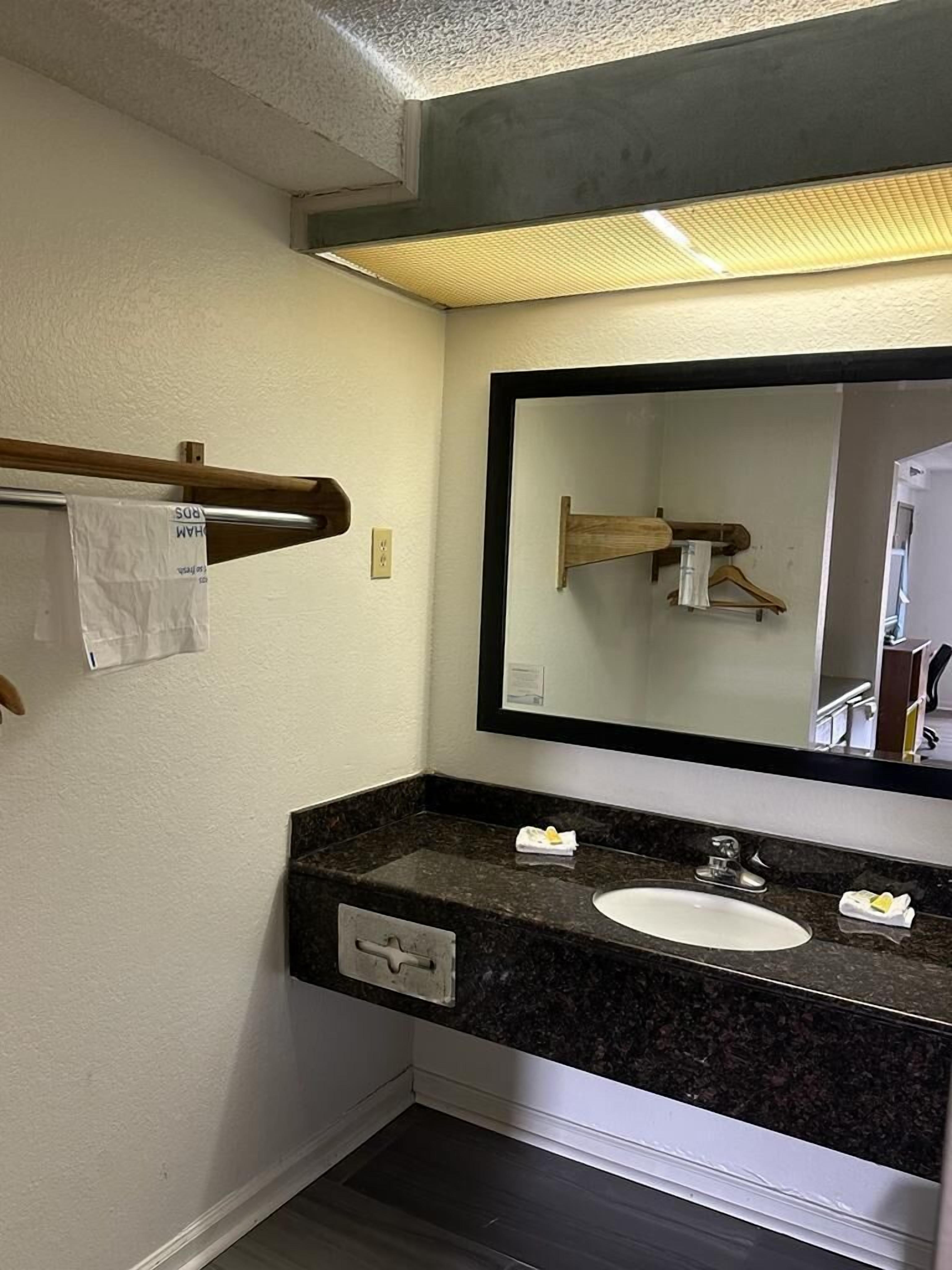 A bathroom with a granite countertop, a white sink, a mirror, and a towel rack.