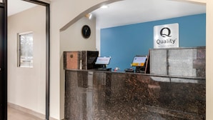 A hotel reception desk with a "Quality by Choice Hotels" sign, a clock, and a computer monitor. - Quality Inn & Suites Decatur - Priceville I-65 (Decatur)