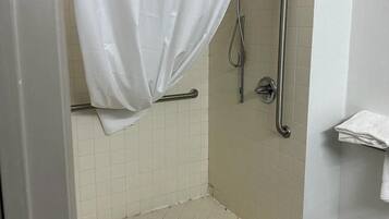 A shower area with a white shower curtain, grab bars, and a handrail.