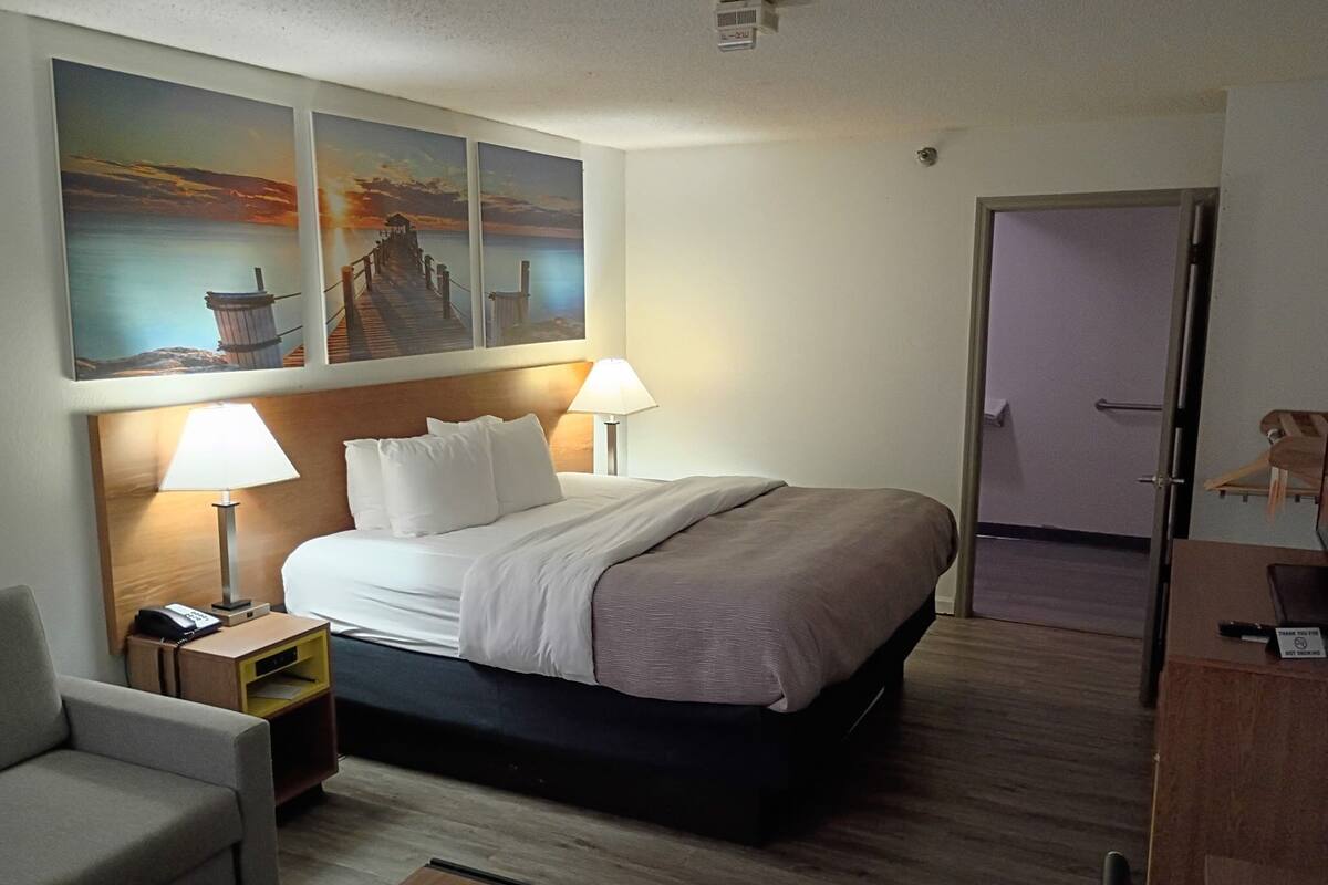 A hotel room with a bed, two bedside lamps, a nightstand, a chair, a desk, and a door.