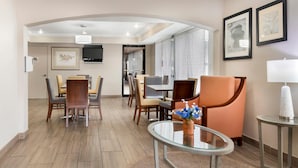 A hotel lobby with a dining area, a TV mounted on the wall, framed artwork, and a modern chandelier. - Quality Inn & Suites Decatur - Priceville I-65 (Decatur)
