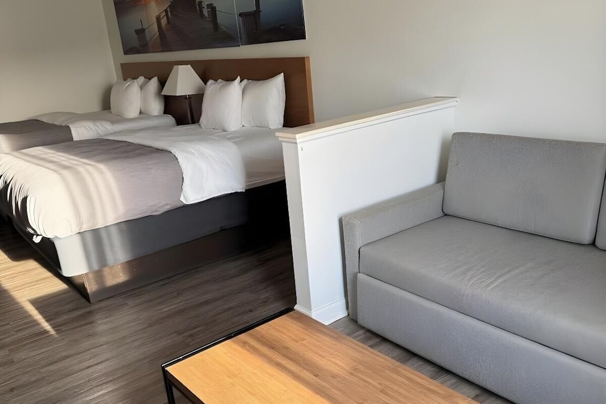 A modern hotel room with a bed, a sofa, a coffee table, and a painting on the wall.