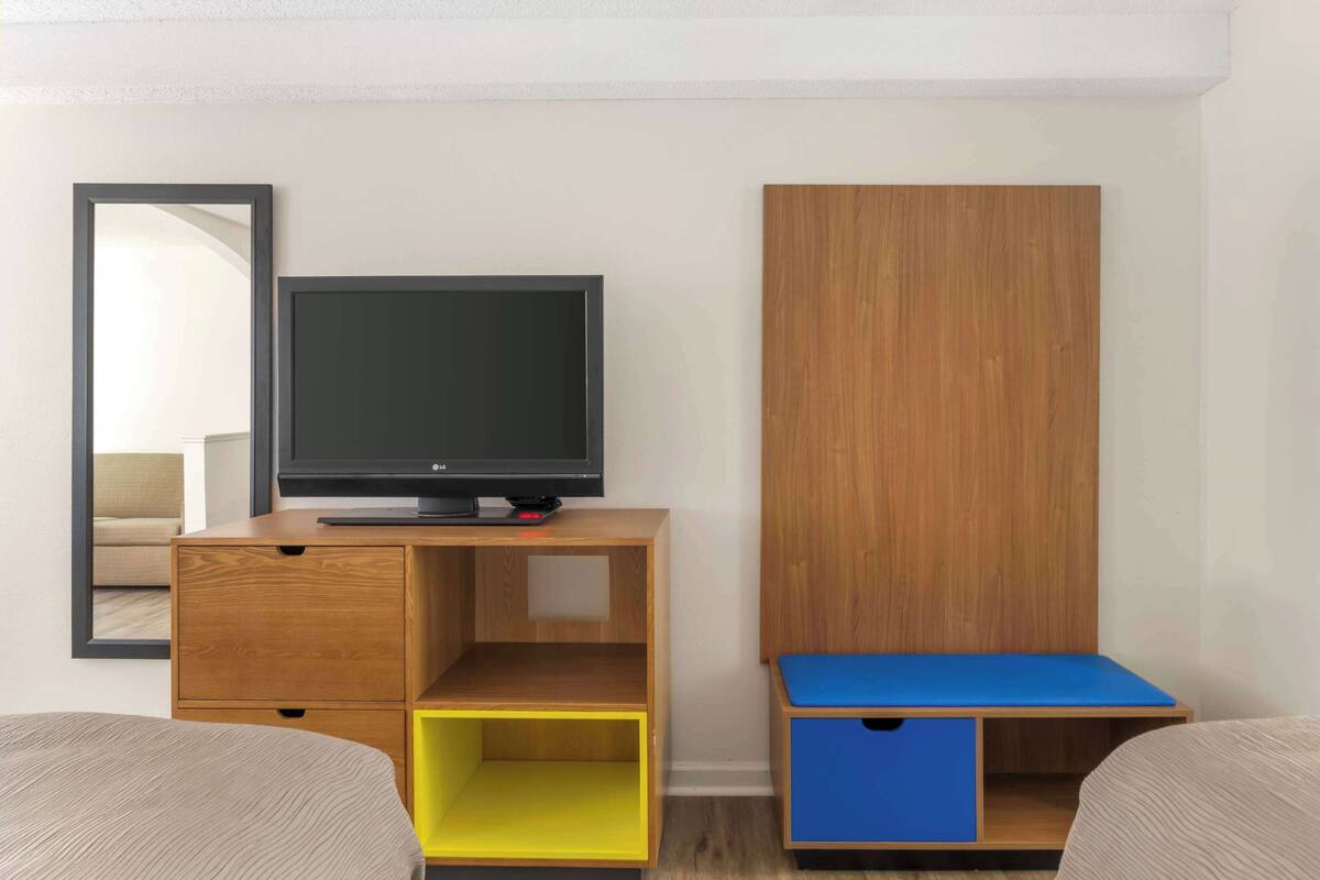 A room with a bed, a TV on a wooden stand, a mirror, and a wardrobe.