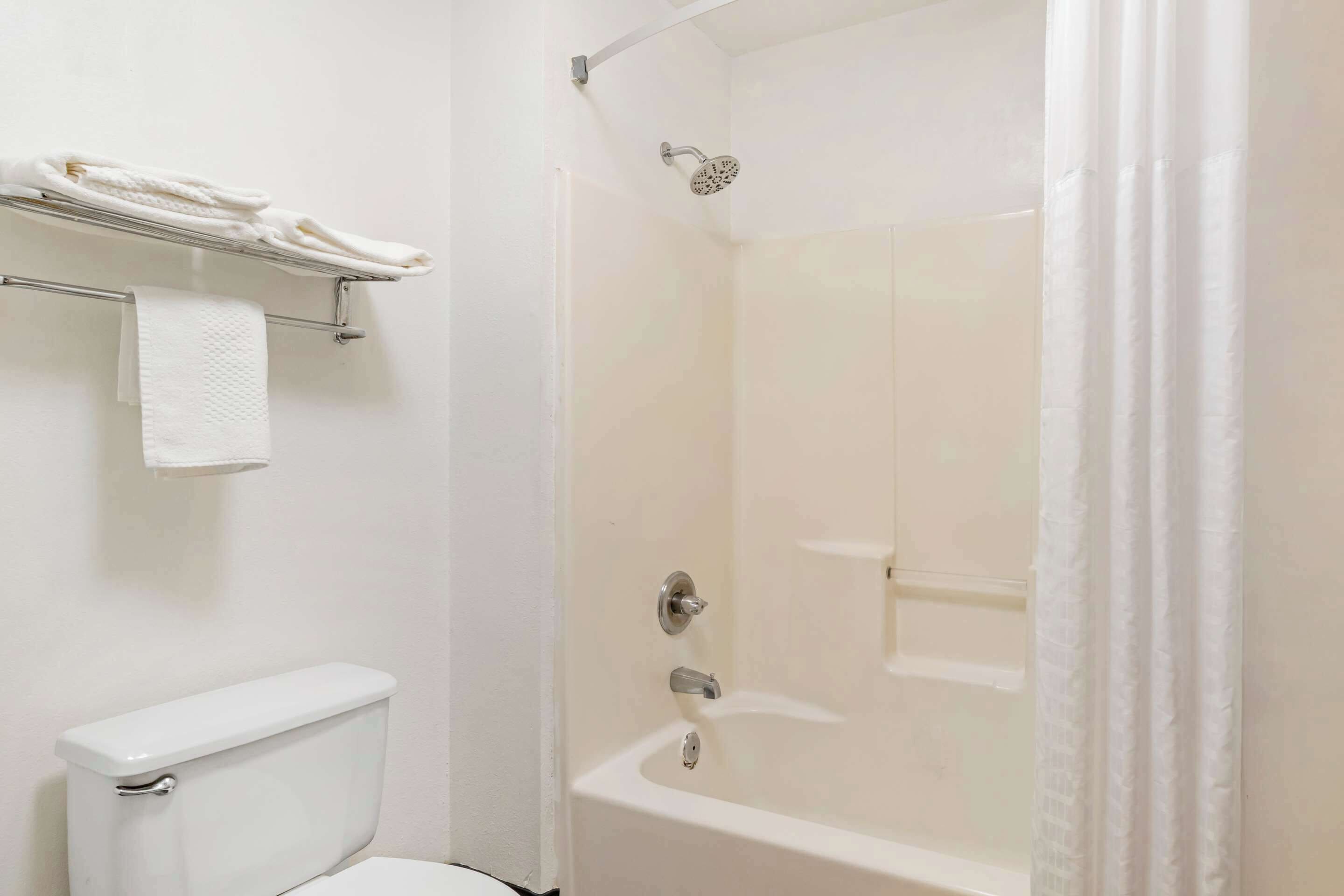 Un baño con inodoro, toallero con toallas dobladas y zona de ducha con cortina.