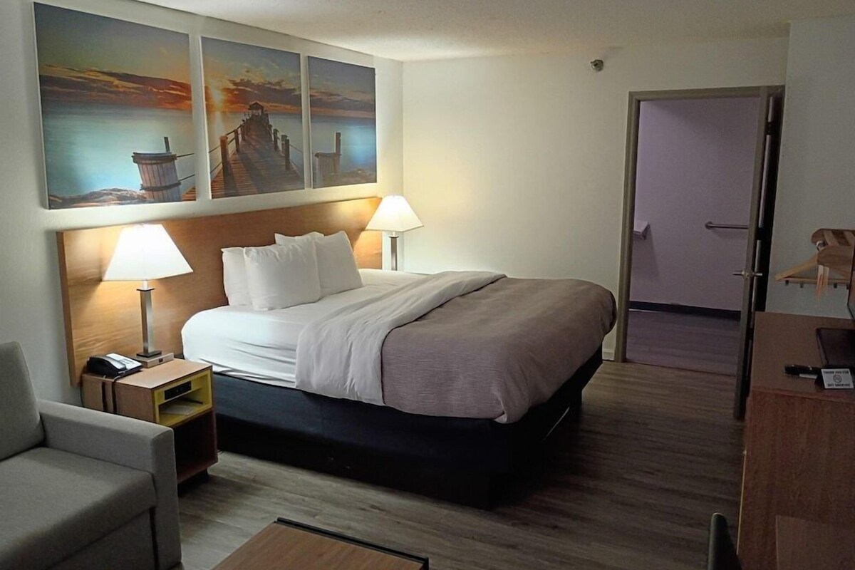A hotel room with a bed, two bedside lamps, a chair, a desk, and artwork on the wall.