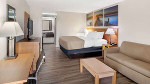 A hotel room with a bed, a sofa, a desk, a TV, and a painting on the wall. - Quality Inn & Suites Decatur - Priceville I-65 (Decatur)