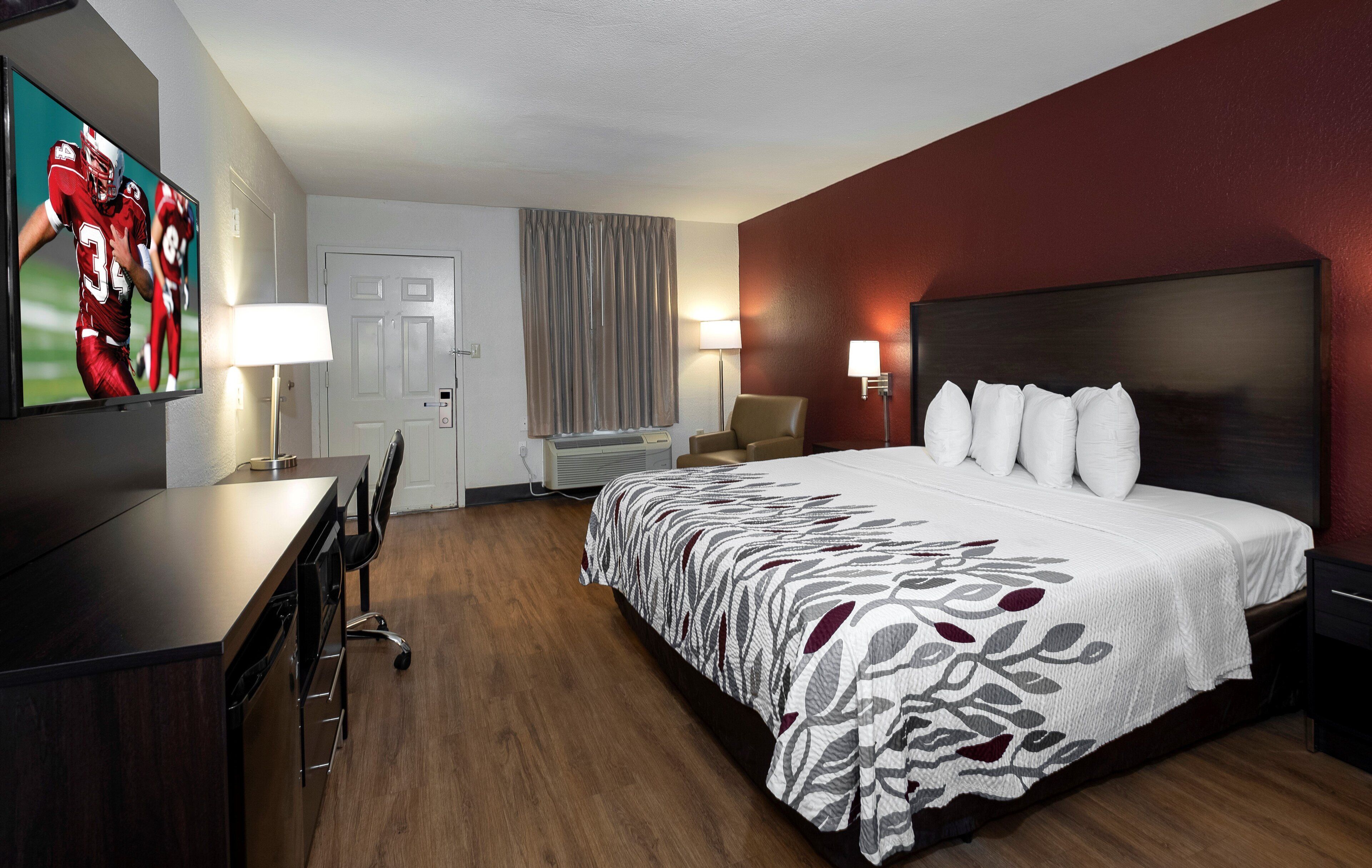 Habitación de hotel con una cama grande, un escritorio, una silla, dos lámparas, una puerta y una ventana con cortinas.