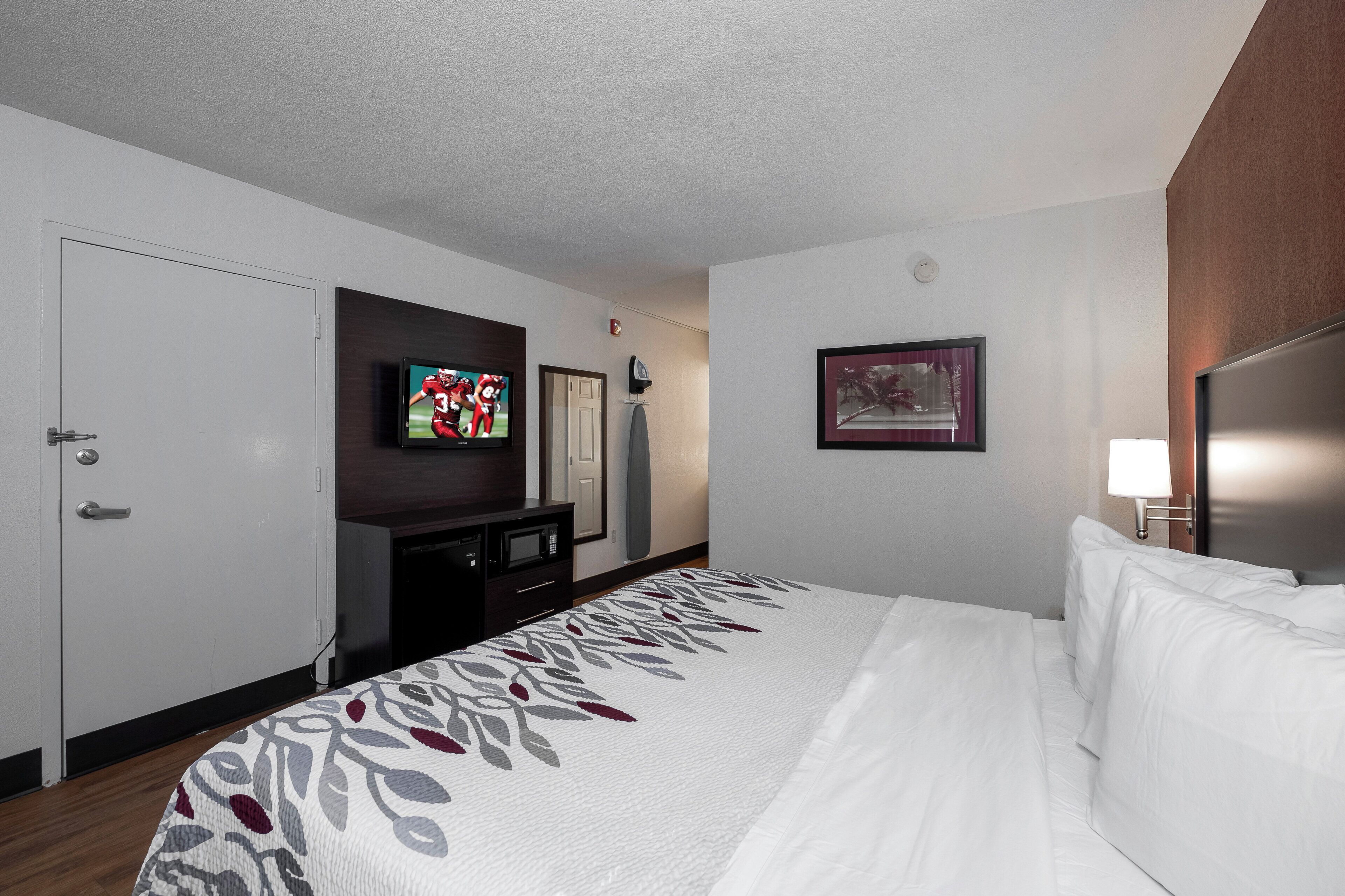 A hotel room with a bed, a television, a desk, and a door.