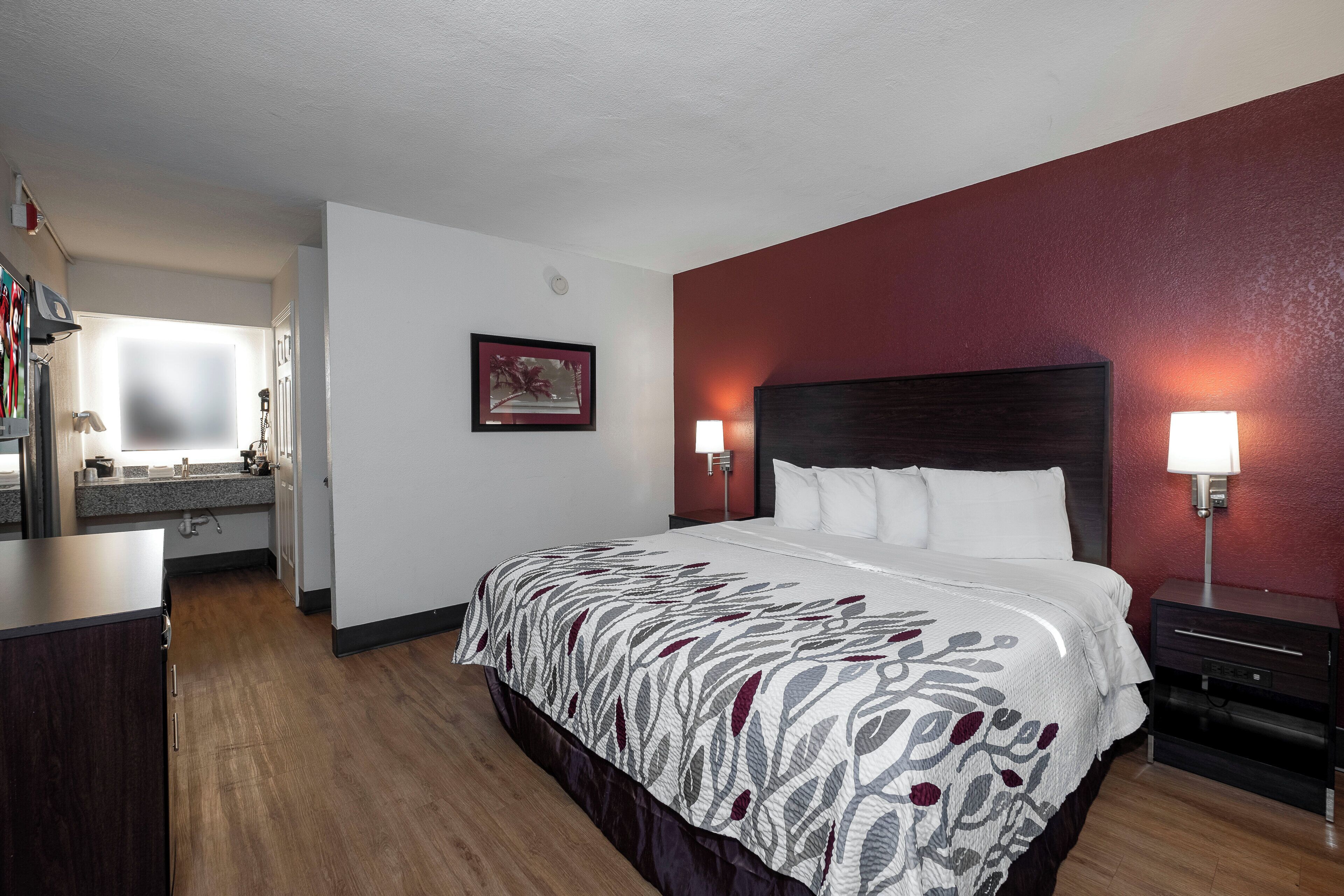 A hotel room with a bed, bedside lamps, a nightstand, a dresser, a mirror, and a framed picture on the wall.