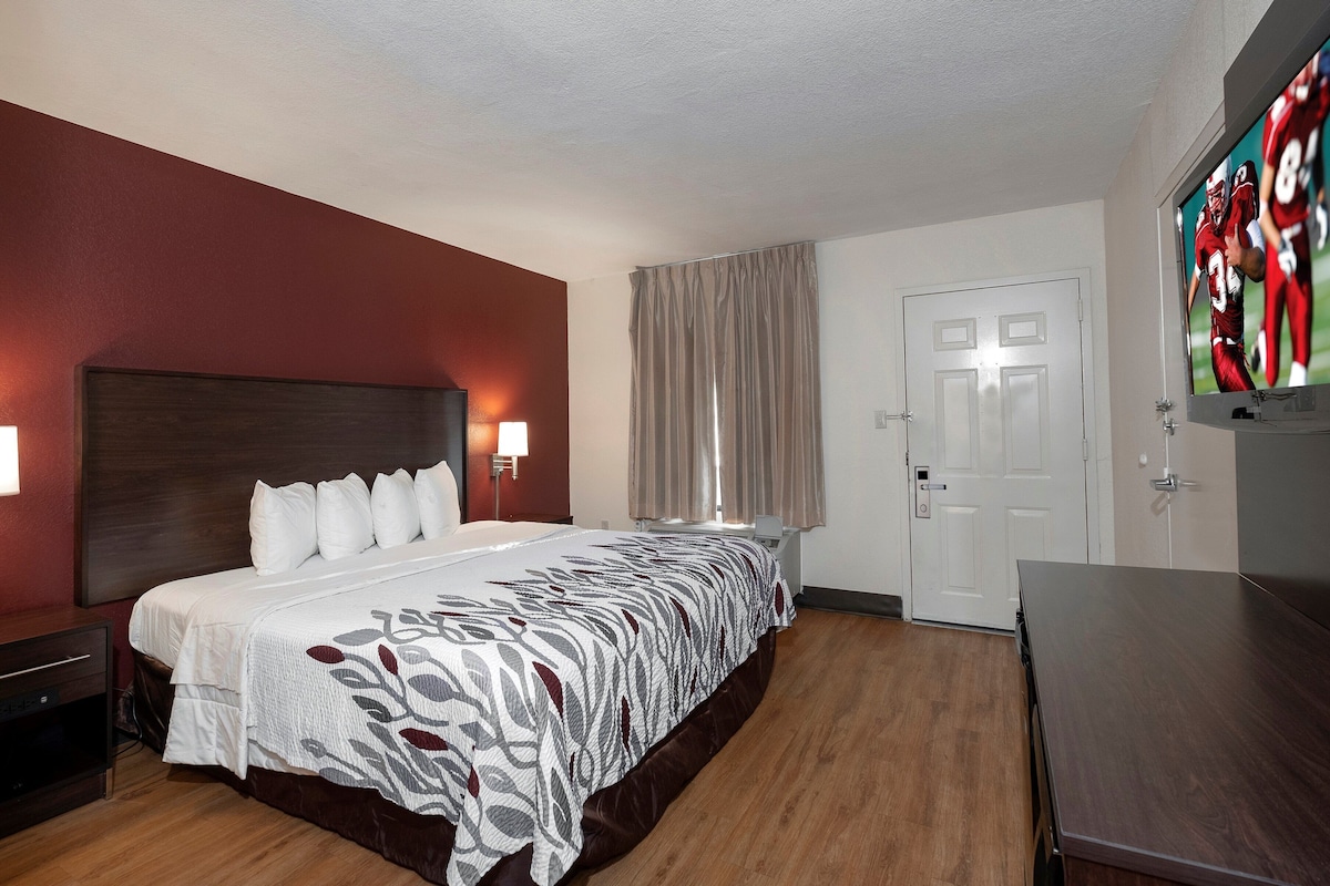 Een hotelkamer met een groot bed, een aan de muur bevestigde televisie, een deur en een nachtkastje.