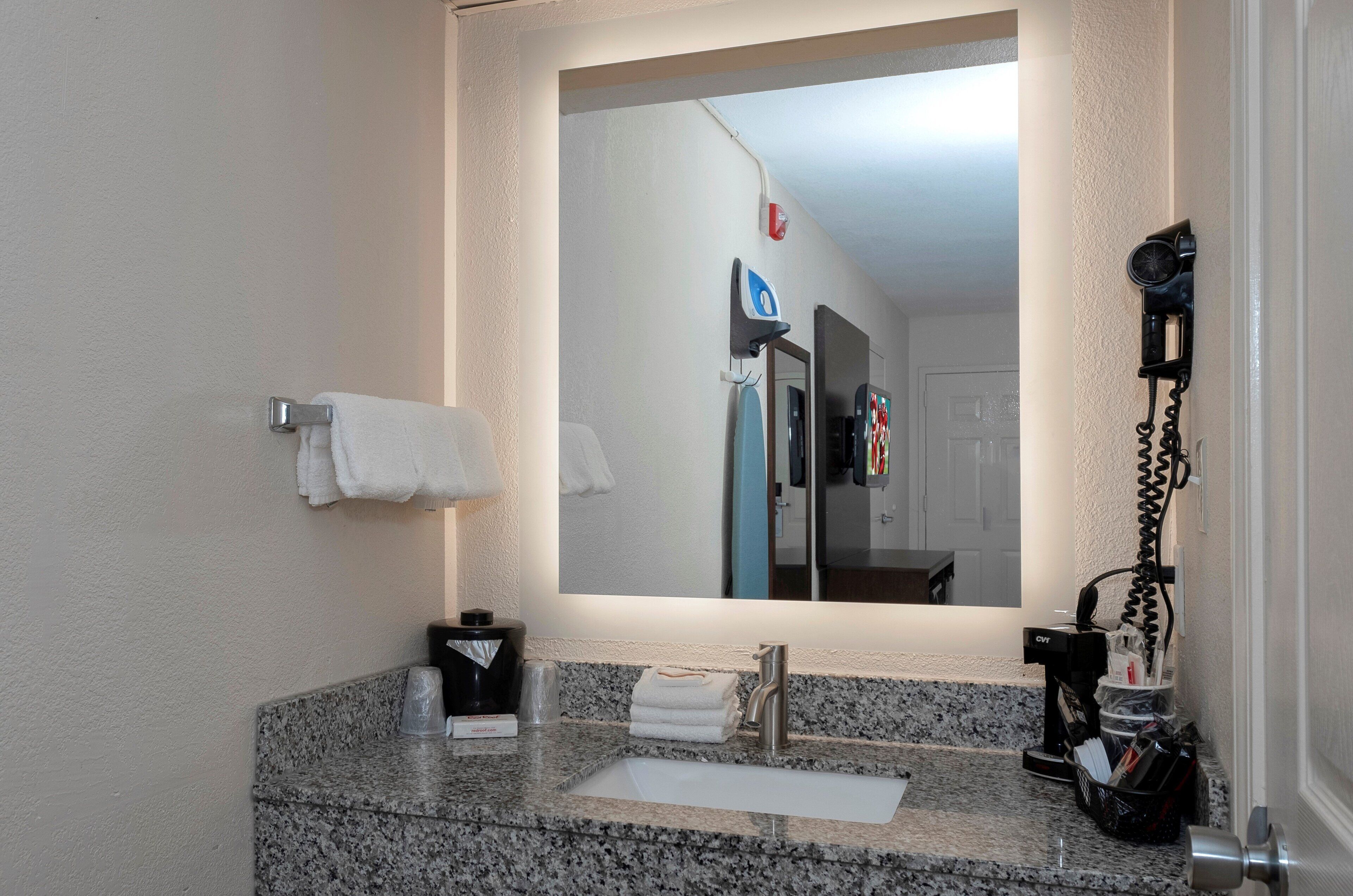 Un baño con encimera de granito, lavamanos, espejo y toallero.