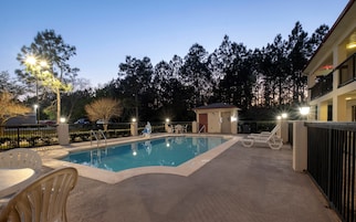 A swimming pool with lounge chairs, a small building, and a fence.