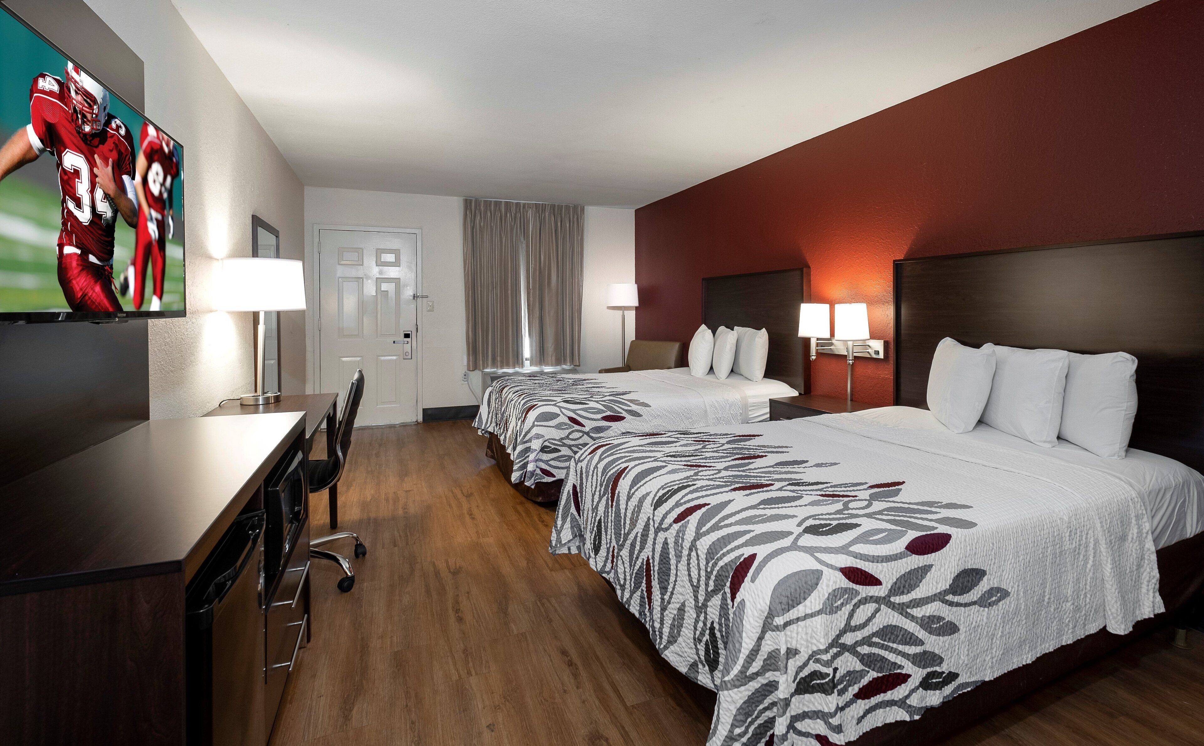 Habitación de hotel con dos camas, un escritorio, una silla, un televisor y una puerta.