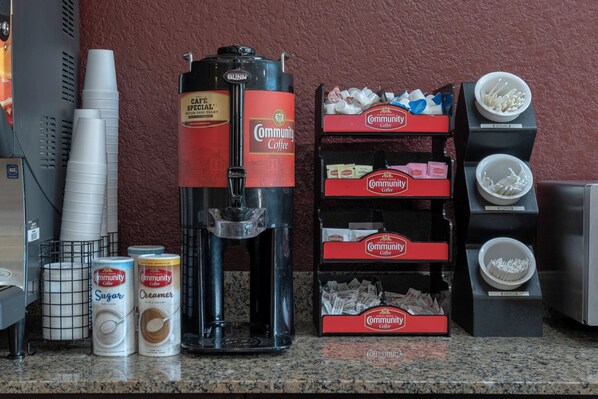 A coffee station with a coffee machine, cups, and containers of sugar and creamer.