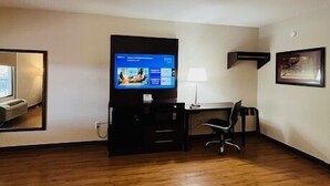 Hotelkamer met houten vloer, een wandtelevisie, bureau met stoel en een klein tafeltje met lamp.
