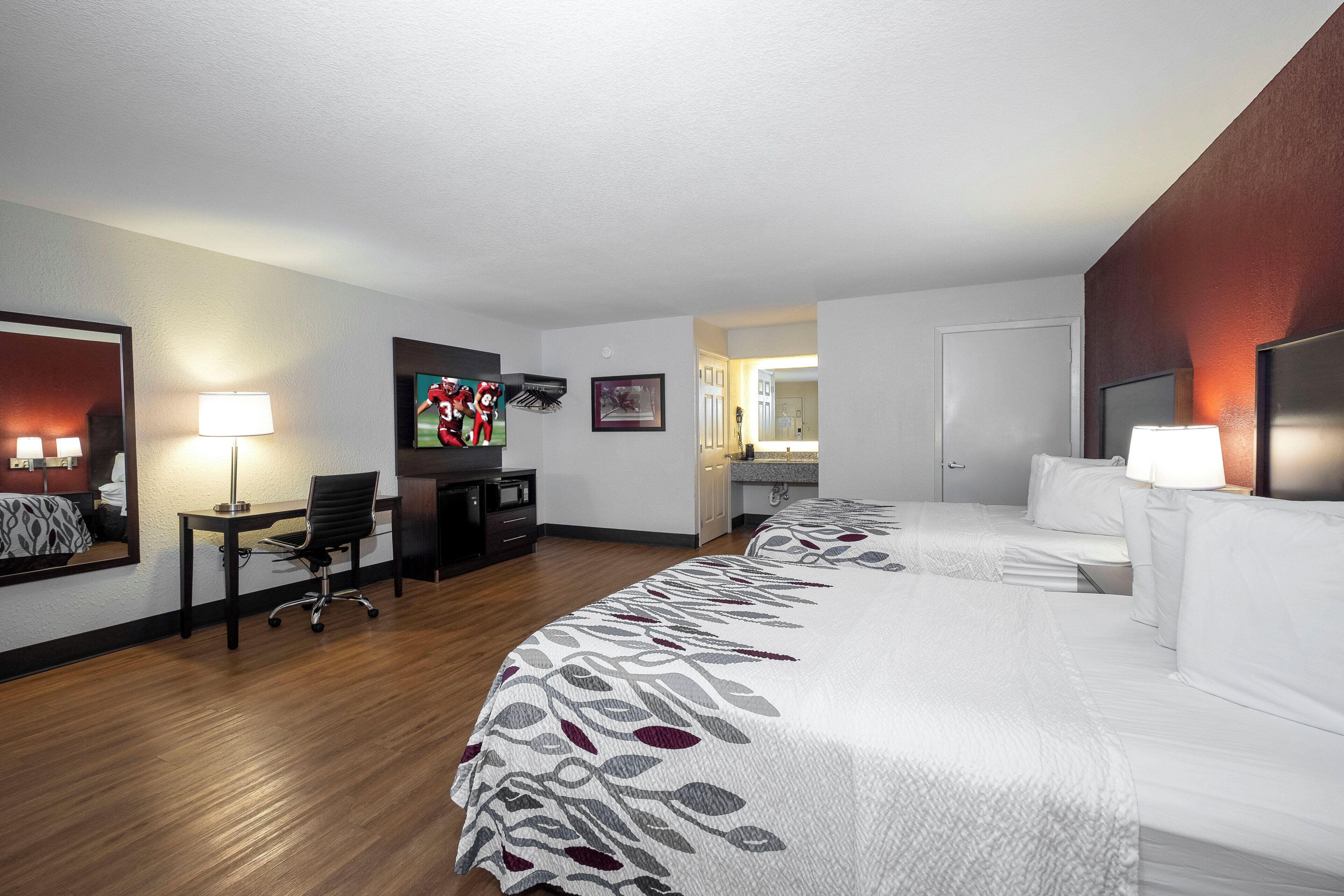 A hotel room with a large bed, a desk with a chair, a television, and a mirror.