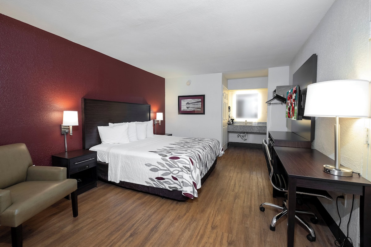 Ein Hotelzimmer mit Bett, Schreibtisch, Stuhl und einem durchgegangenen Tür sichtbaren Badezimmer.