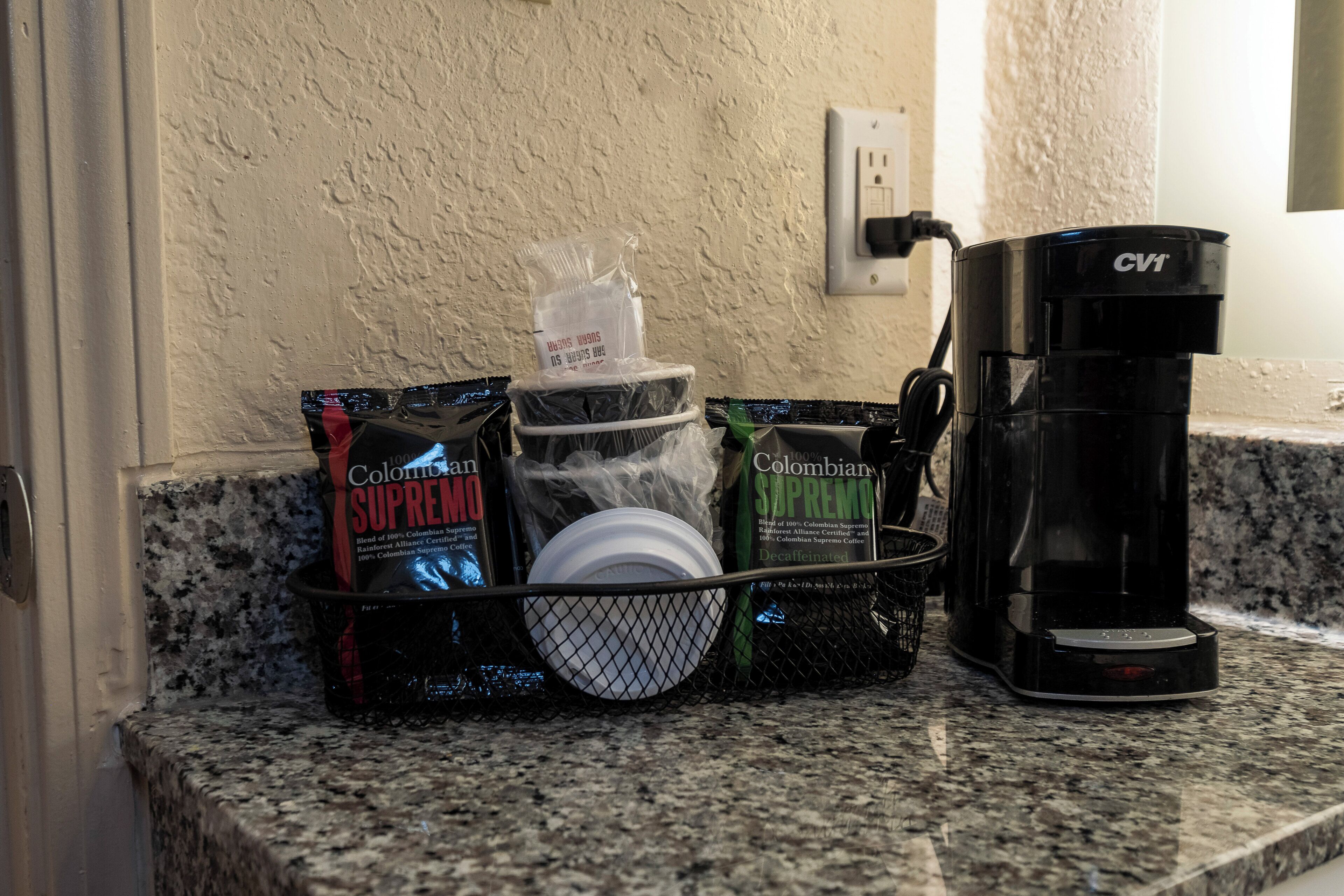 A kitchen counter with a coffee maker, a basket containing coffee pods, and a dish rack.