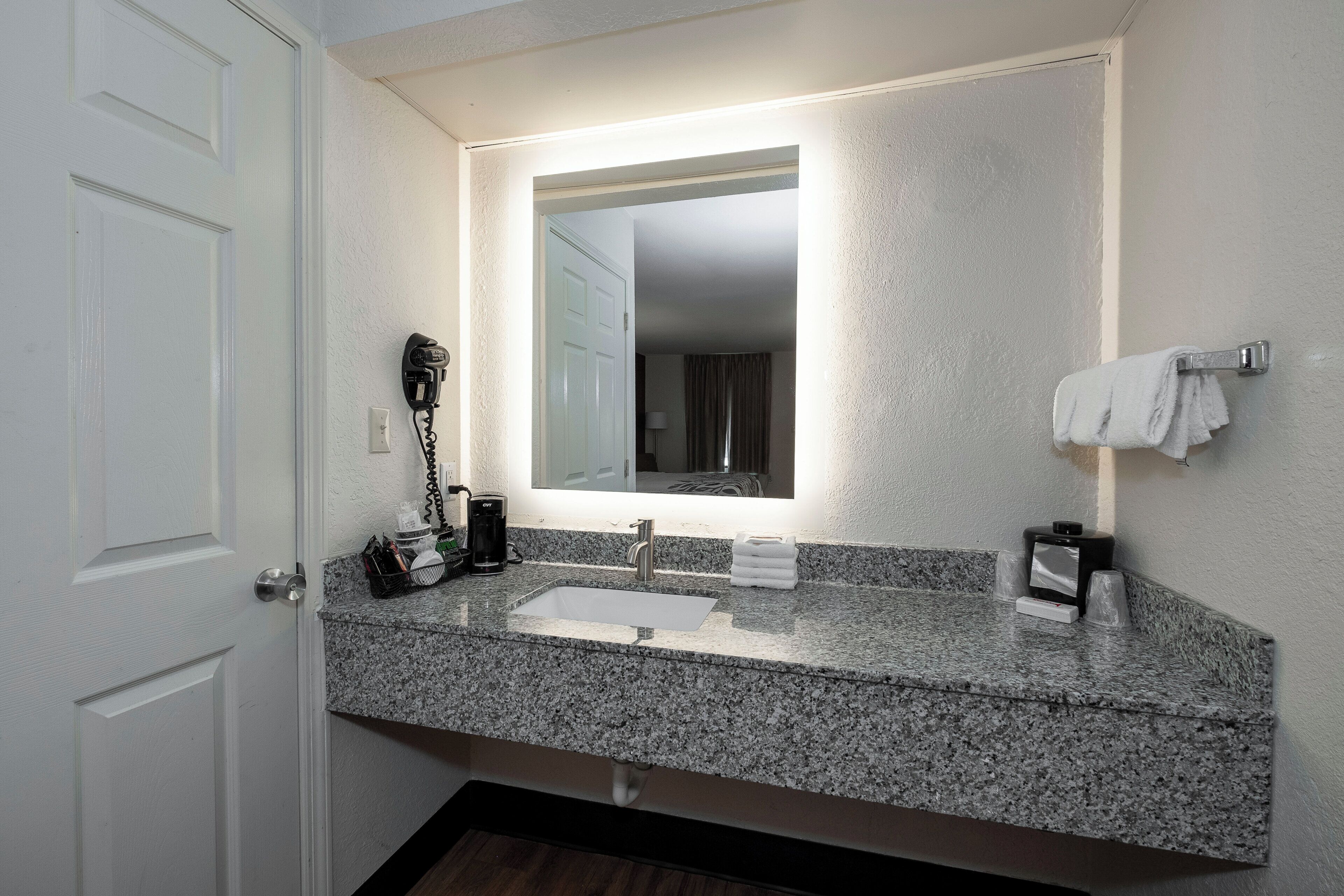 A bathroom with a granite countertop, a sink, a mirror, a hairdryer, and a towel rack.