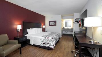 A hotel room with a bed, desk, chair, and a bathroom visible through an open door.