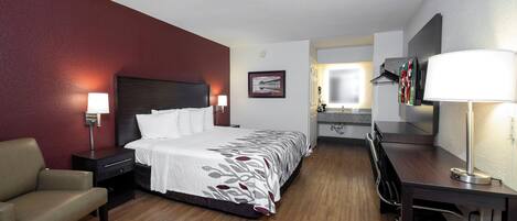 A hotel room with a bed, desk, chair, and a bathroom visible through an open door.