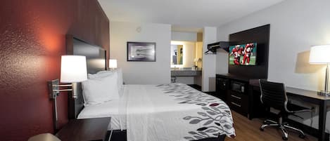 A hotel room with a bed, desk, chair, TV, and a small kitchenette.