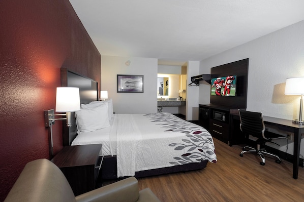 A hotel room with a bed, desk, chair, TV, and a small kitchenette. - Red Roof Inn Gulf Shores (Gulf Shores)
