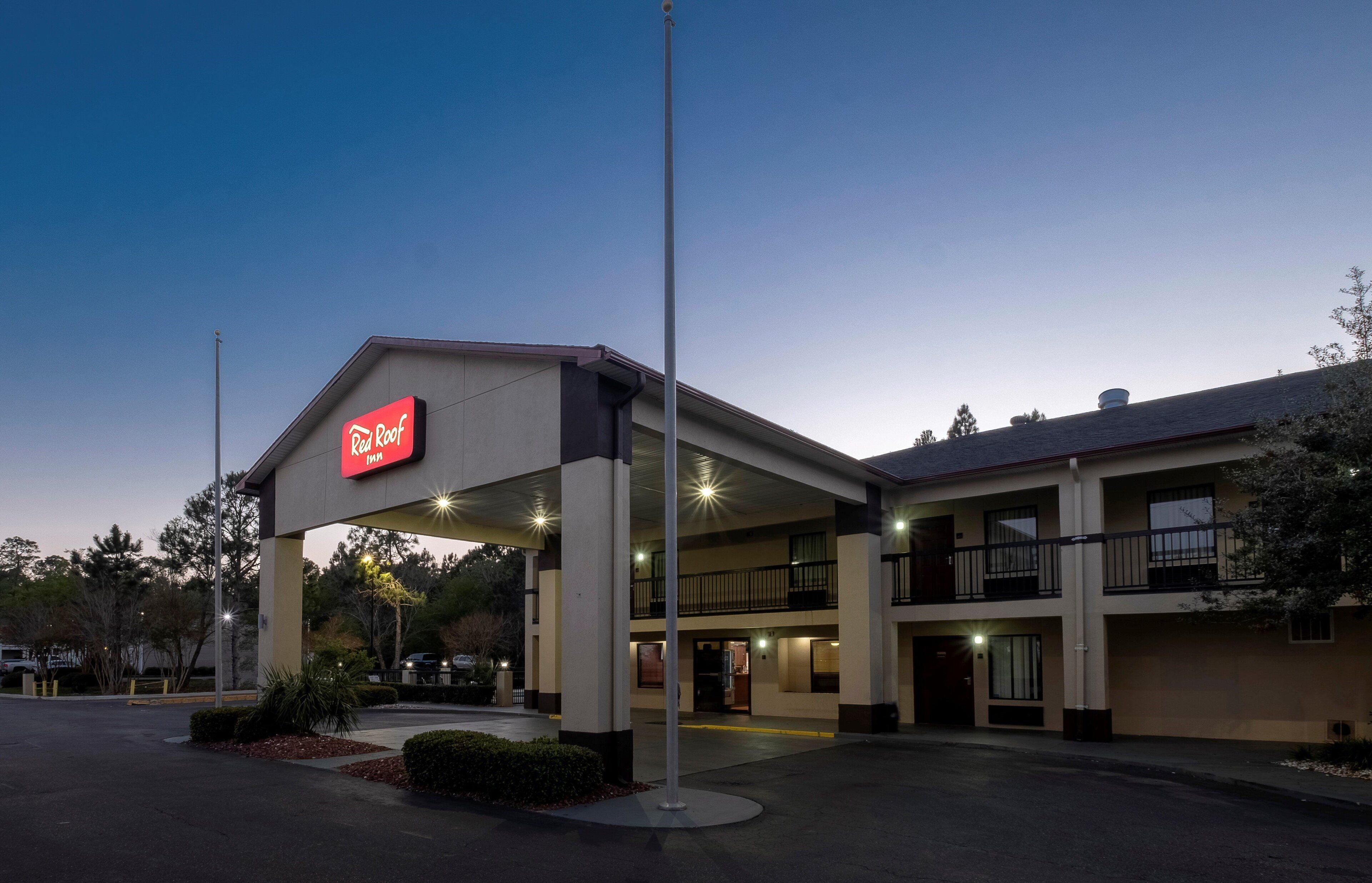 A Red Roof Inn with a two-story structure, a covered parking area, and a clear sky.