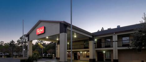 Un hotel Red Roof Inn con una estructura de dos pisos, un área de estacionamiento techada y cielo despejado.