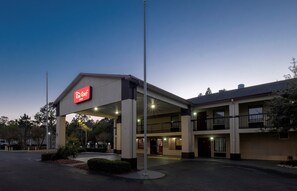 Un hôtel Red Roof Inn avec un bâtiment à deux étages, un espace de stationnement couvert et un ciel dégagé.