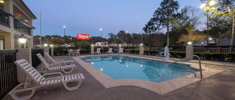 Una piscina con sillas de descanso y un cartel de Red Roof Inn al fondo.