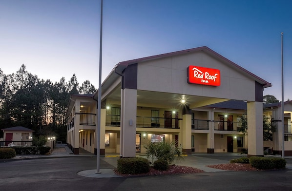 Un Red Roof Inn de dos pisos, con asientos exteriores y una entrada bien iluminada.
