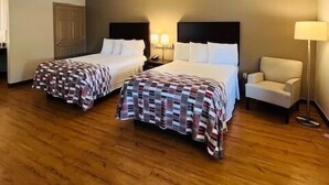 Een hotelkamer met twee bedden, een stoel, een lamp en een houten vloer.