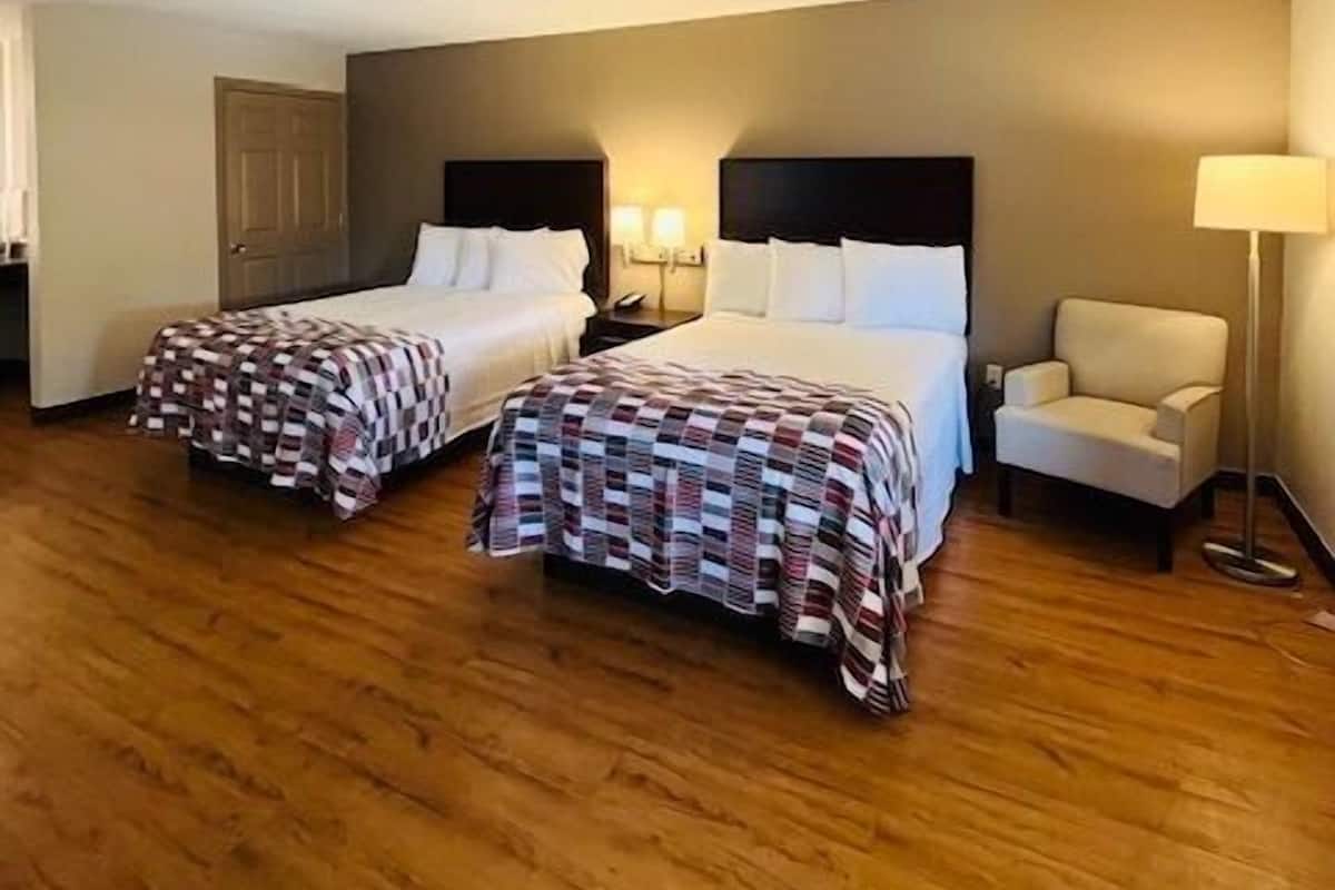 Ein Hotelzimmer mit zwei Betten, einem Sessel, einer Lampe und Holzboden.