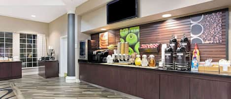 Eine Hotelhalle mit einer Rezeption, einem großen Fernsehbildschirm und einer Kaffeestation.
