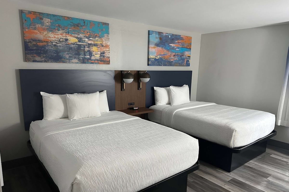 Een hotelkamer met twee bedden, een nachtkastje en twee abstracte schilderijen aan de muur.
