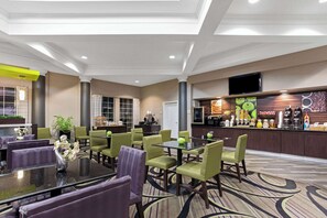 Un vestíbulo de hotel con asientos verdes y morados, una barra de café y una pantalla grande en la pared.