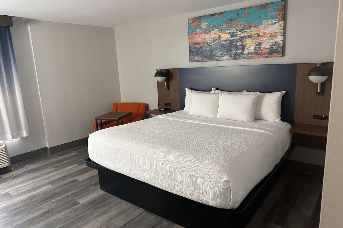 Een hotelkamer met een groot bed, een klein tafeltje, twee stoelen, een schilderij aan de muur en een plafondlamp.
