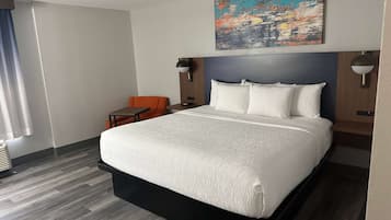 A hotel room with a large bed, a small table, two chairs, a painting on the wall, and a ceiling lamp.
