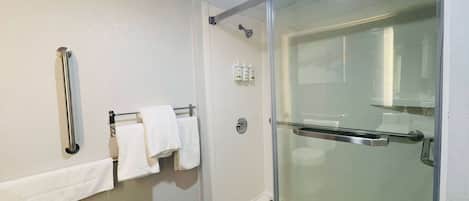 Un baño moderno con cabina de ducha de vidrio, un perchero con toallas blancas y un secamanos empotrado en la pared.