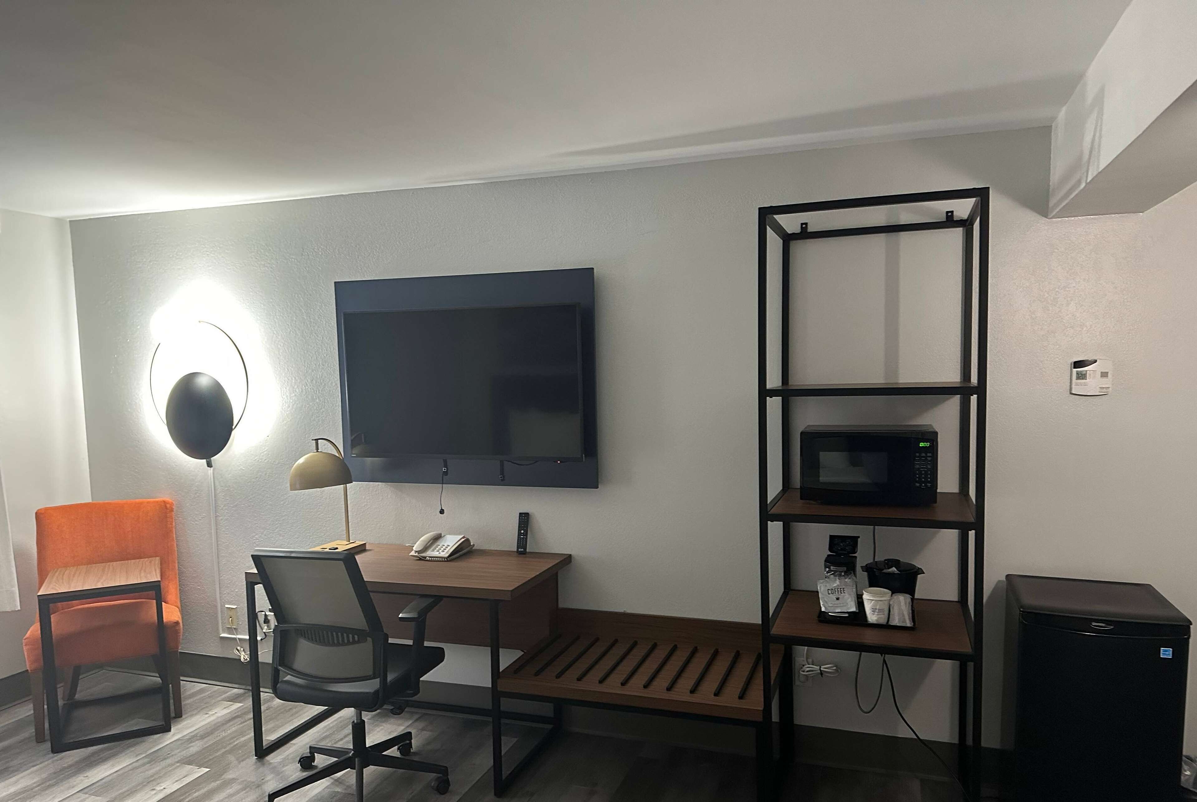 Ein kompaktes Hotelzimmer mit Schreibtisch, Stuhl, Fernseher, Mikrowelle und einer kleinen Küchenzeile.