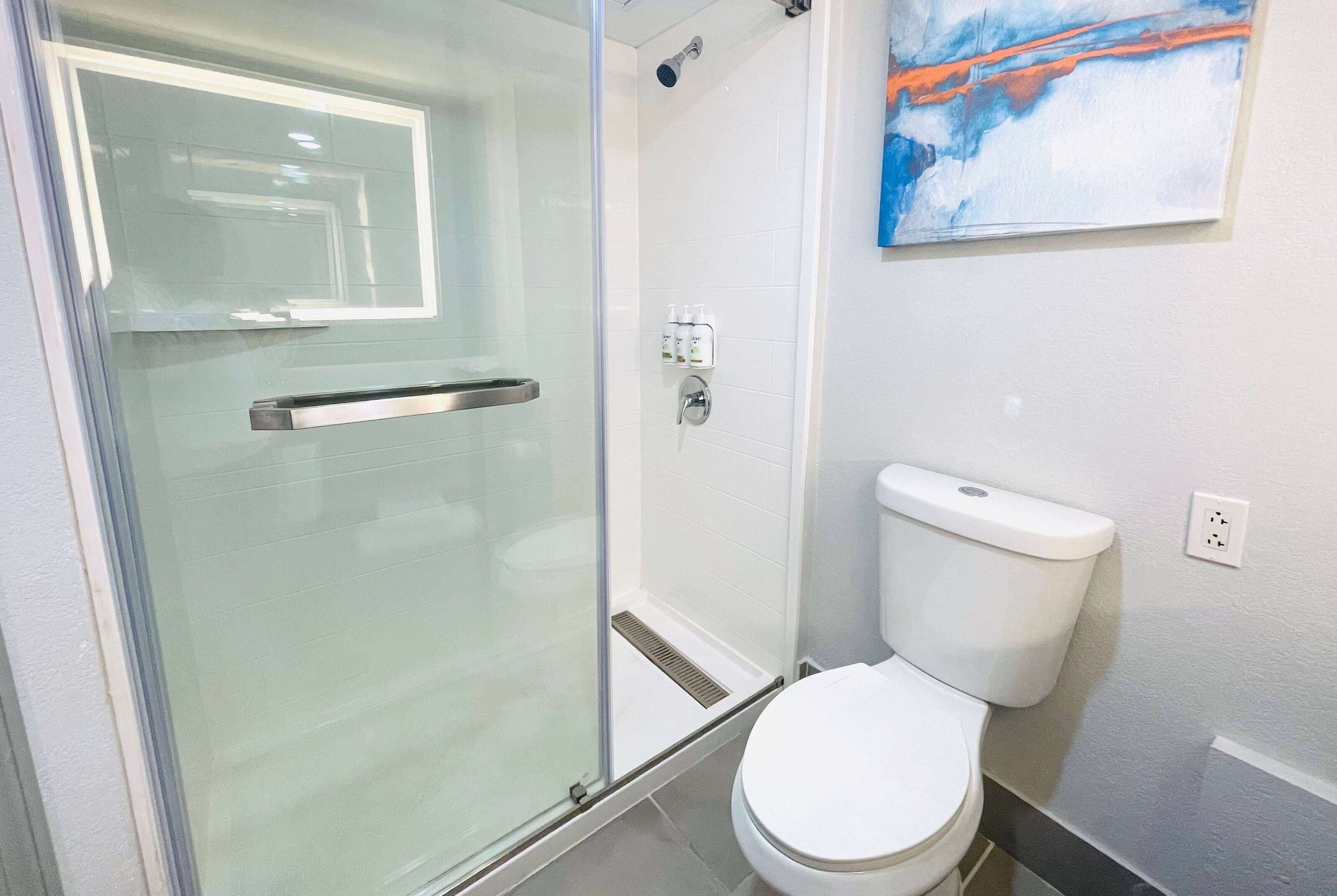 A bathroom with a glass shower enclosure, a white toilet, and a wall-mounted painting.
